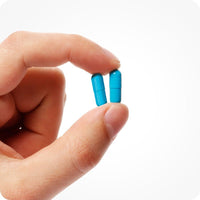 For Men's Fertility Support Bundle the image of a man's left hand on the left side of the frame on a white background. The man is holding two capsules of Conceive Plus Men Fertility Support with his index finger and thumb