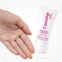 For Men's Fertility Support Bundle the image of a tube of Conceive Plus Fertility Lubricant 30ml on the right side of the frame while a woman left hand entering the frame from the left side on a white background. The woman hand has some lube on its palm with fingers closed.