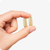 Hand holding two beige Conceive Plus Prenatal with DHA capsules, showing their compact vegan form for daily pregnancy nutrition support.